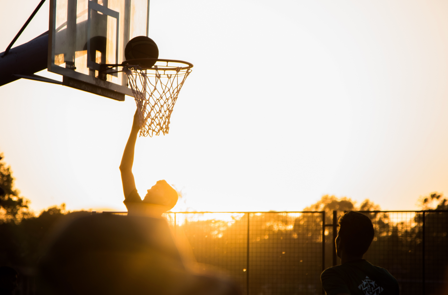 Young man shooting a basketball with sun in the background